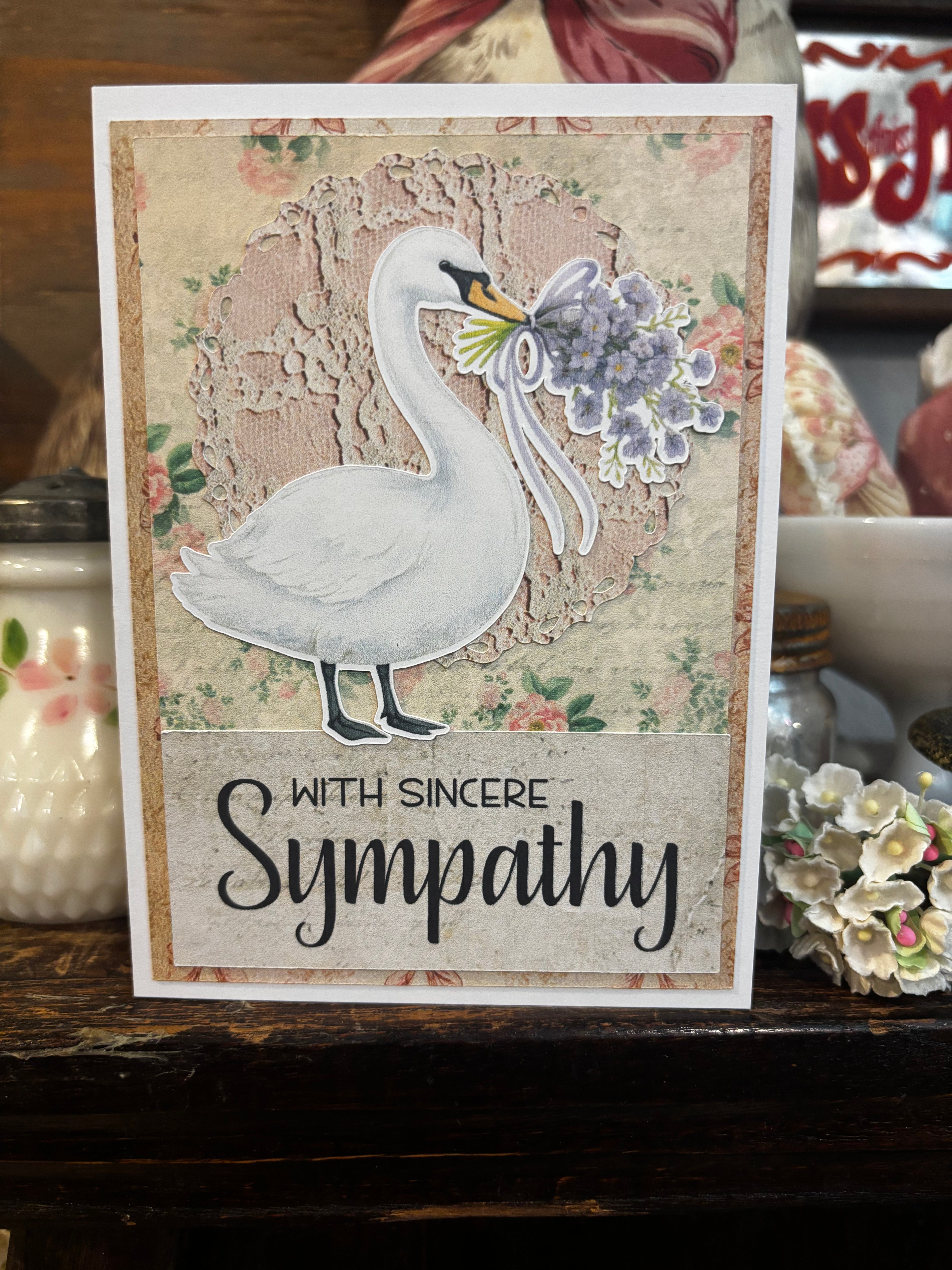 Sympathy card with a swan and flowers on a decorative surface with the text "With Sincere Sympathy" on it. 