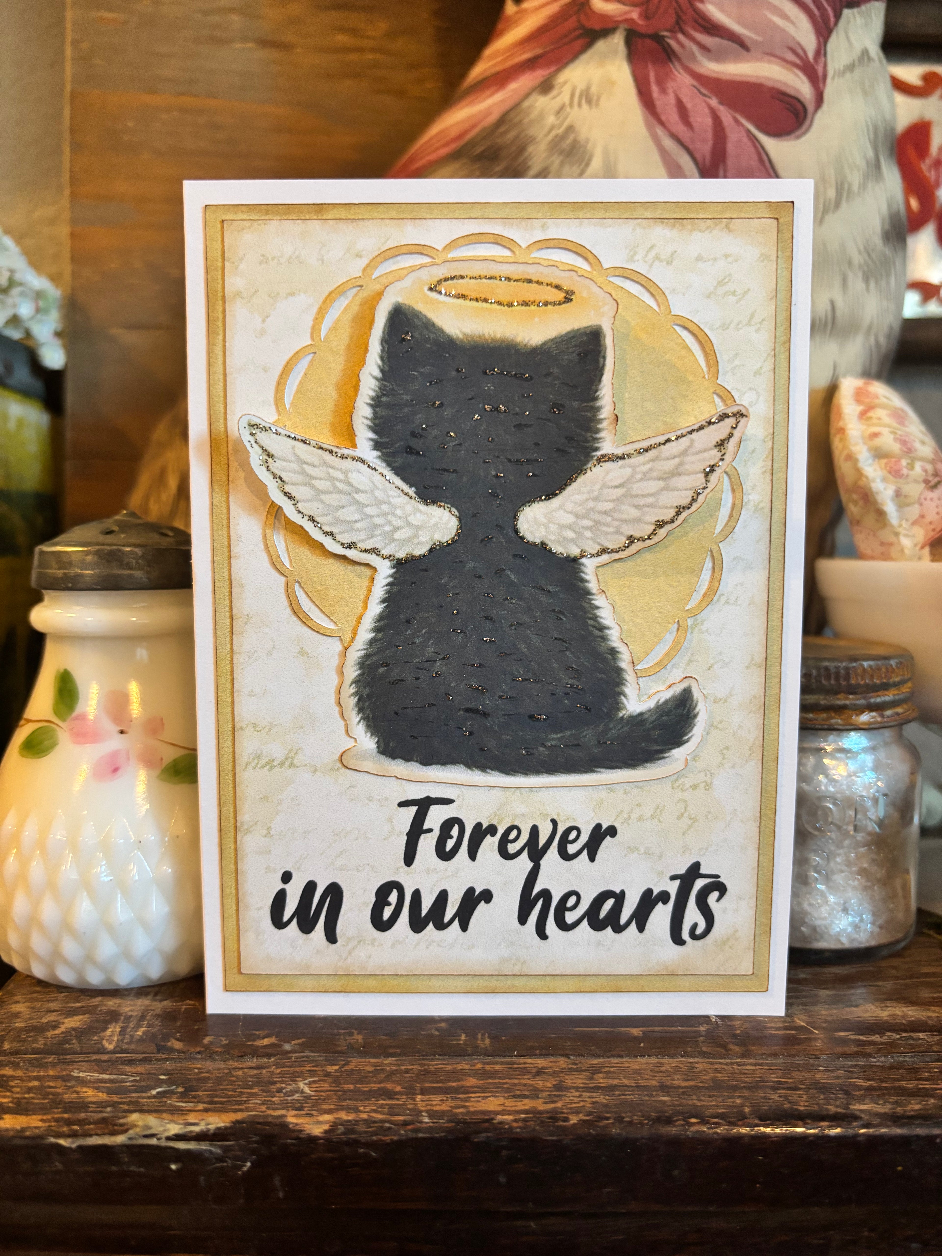 Memorial card with a cat with angel wings and a halo illustration and the text 'Forever in our hearts'. 